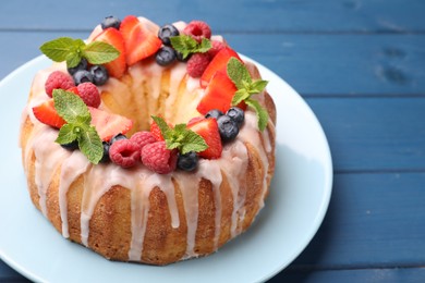 Photo of Delicious bundt cake with berries, glaze and mint on blue wooden table, closeup