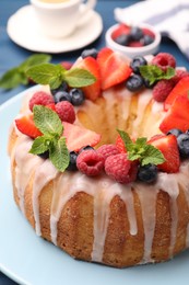 Photo of Delicious bundt cake with berries, glaze and mint on blue table, closeup
