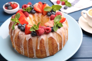 Photo of Delicious bundt cake with berries, glaze and mint on blue wooden table, closeup