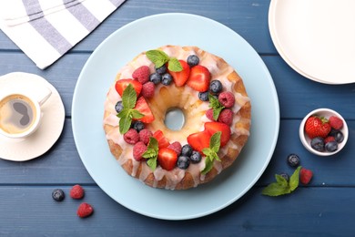 Photo of Delicious bundt cake with berries, glaze, mint and cup of coffee on blue wooden table, flat lay