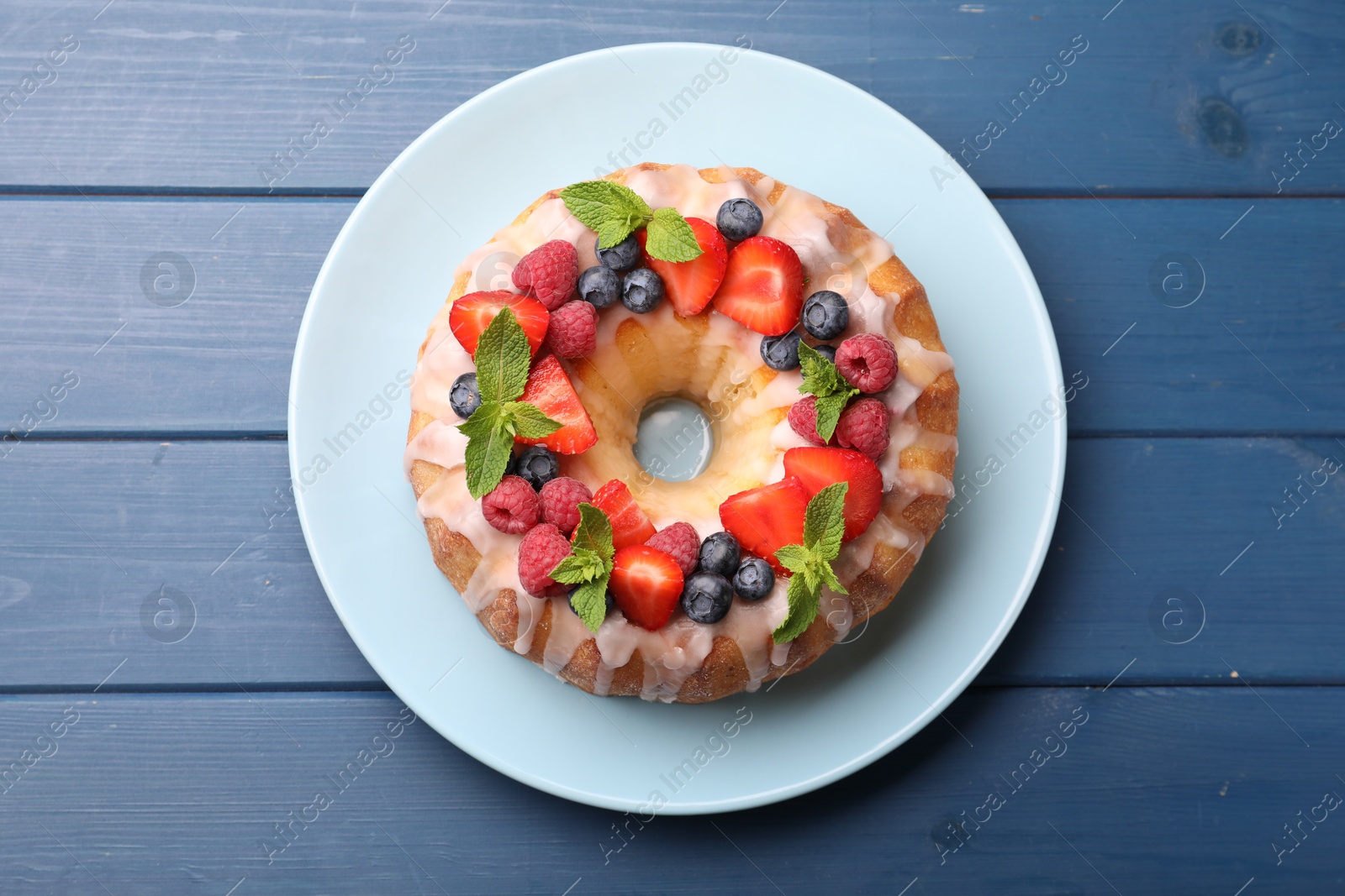 Delicious bundt cake with berries, glaze and mint on blue wooden table, top view Photo of Delicious bundt cake with berries, glaze and mint on blue wooden table, top view