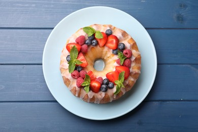 Photo of Delicious bundt cake with berries, glaze and mint on blue wooden table, top view
