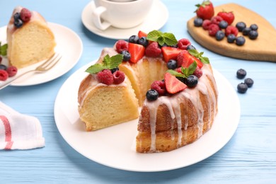 Photo of Pieces of delicious bundt cake with berries, glaze and mint on light blue wooden table, closeup