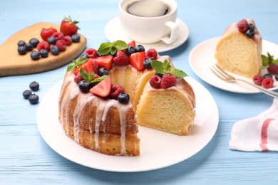 Photo of Pieces of delicious bundt cake with berries, glaze and mint on light blue wooden table, closeup