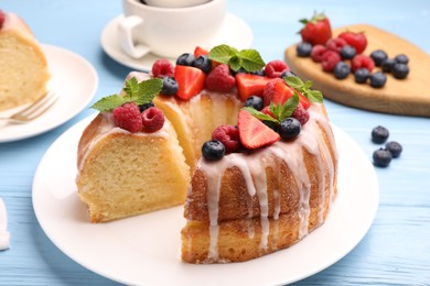Photo of Pieces of delicious bundt cake with berries, glaze and mint on light blue wooden table, closeup