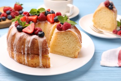 Photo of Pieces of delicious bundt cake with berries, glaze and mint on light blue wooden table, closeup