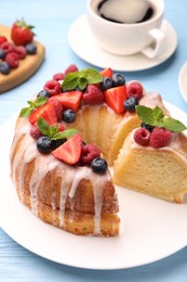Photo of Pieces of delicious bundt cake with berries, glaze and mint on light blue wooden table, closeup