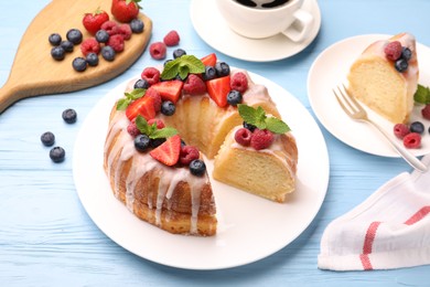 Photo of Pieces of delicious bundt cake with berries, glaze and mint on light blue wooden table