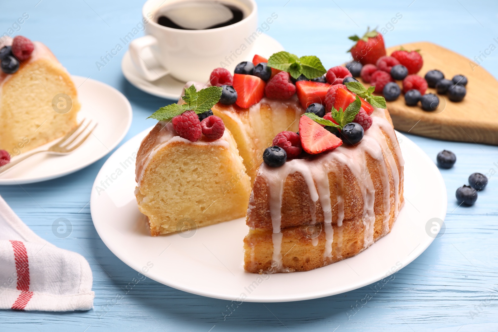 Pieces of delicious bundt cake with berries, glaze and mint on light blue wooden table, closeup Photo of Pieces of delicious bundt cake with berries, glaze and mint on light blue wooden table, closeup