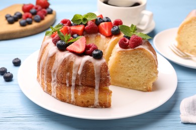 Photo of Pieces of delicious bundt cake with berries, glaze and mint on light blue wooden table, closeup