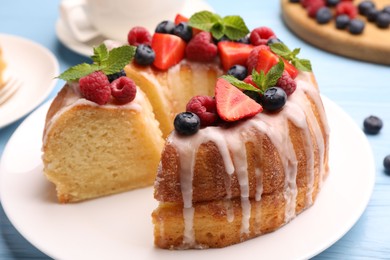 Photo of Pieces of delicious bundt cake with berries, glaze and mint on light blue wooden table, closeup