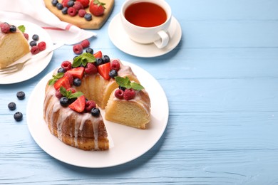 Photo of Pieces of delicious bundt cake with berries, glaze and mint on light blue wooden table