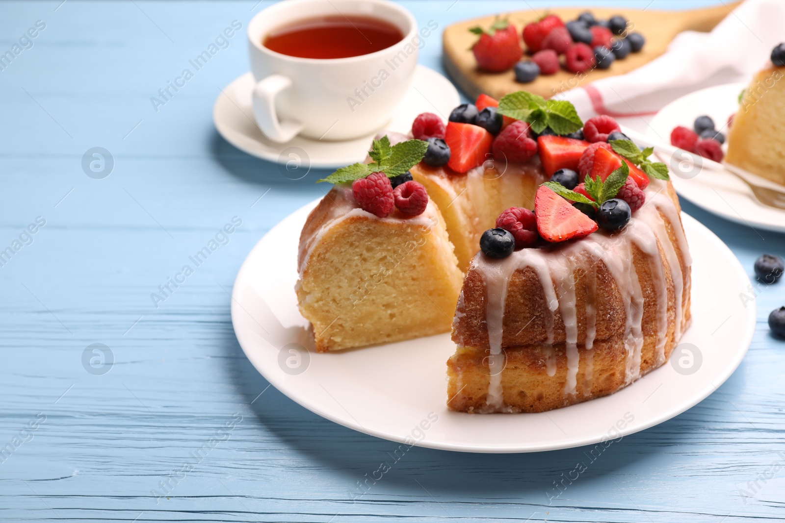 Pieces of delicious bundt cake with berries, glaze and mint on light blue wooden table, closeup Photo of Pieces of delicious bundt cake with berries, glaze and mint on light blue wooden table, closeup