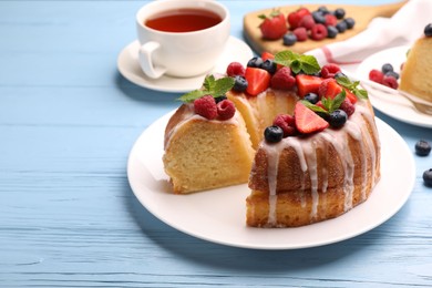 Photo of Pieces of delicious bundt cake with berries, glaze and mint on light blue wooden table, closeup