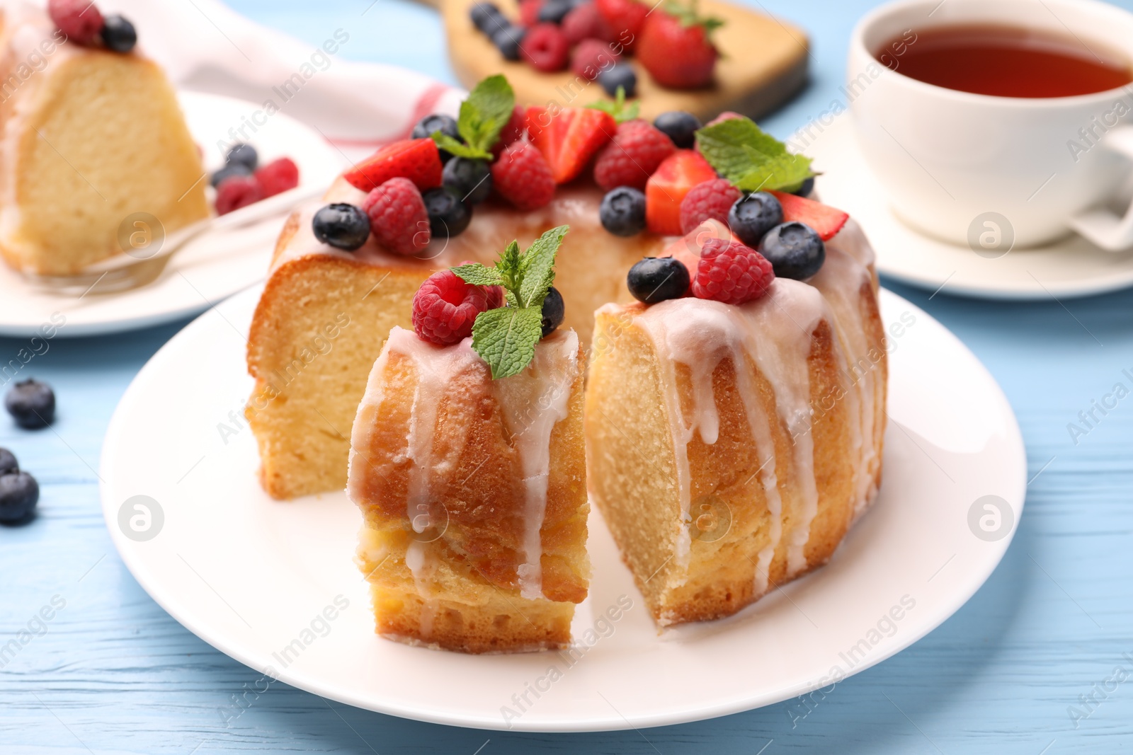Pieces of delicious bundt cake with berries, glaze and mint on light blue wooden table, closeup Photo of Pieces of delicious bundt cake with berries, glaze and mint on light blue wooden table, closeup