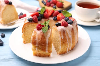 Photo of Pieces of delicious bundt cake with berries, glaze and mint on light blue wooden table, closeup
