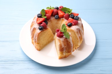 Photo of Pieces of delicious bundt cake with berries, glaze and mint on light blue wooden table, closeup