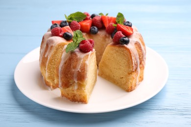Photo of Pieces of delicious bundt cake with berries, glaze and mint on light blue wooden table, closeup