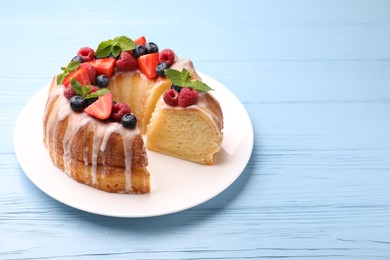 Photo of Pieces of delicious bundt cake with berries, glaze and mint on light blue wooden table, closeup