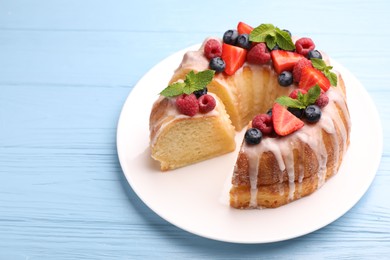 Photo of Pieces of delicious bundt cake with berries, glaze and mint on light blue wooden table, closeup