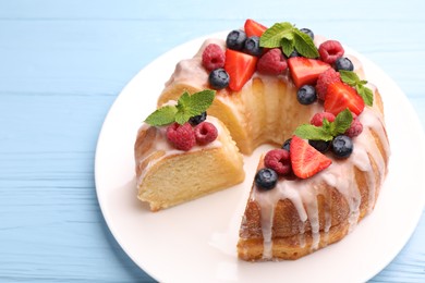 Photo of Pieces of delicious bundt cake with berries, glaze and mint on light blue wooden table, closeup