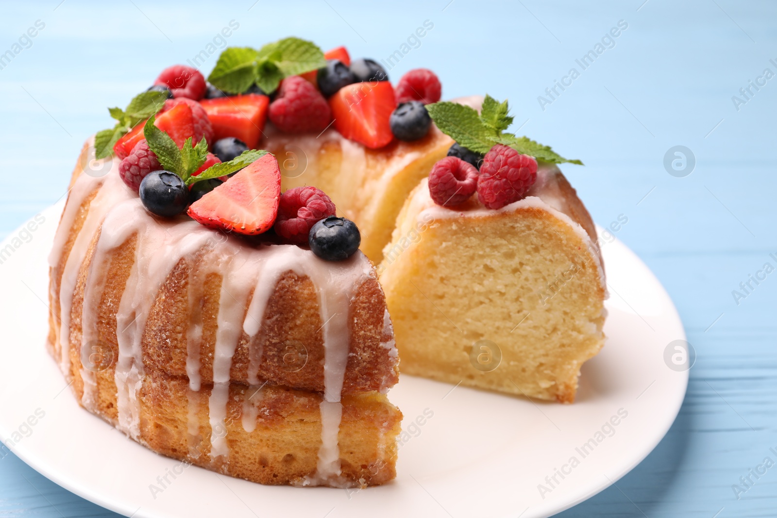 Pieces of delicious bundt cake with berries, glaze and mint on light blue wooden table, closeup Photo of Pieces of delicious bundt cake with berries, glaze and mint on light blue wooden table, closeup