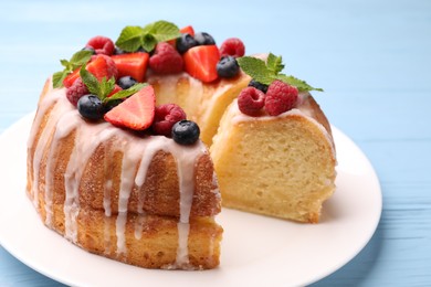 Photo of Pieces of delicious bundt cake with berries, glaze and mint on light blue wooden table, closeup