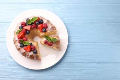 Photo of Pieces of delicious bundt cake with berries, glaze and mint on light blue wooden table, top view. Space for text