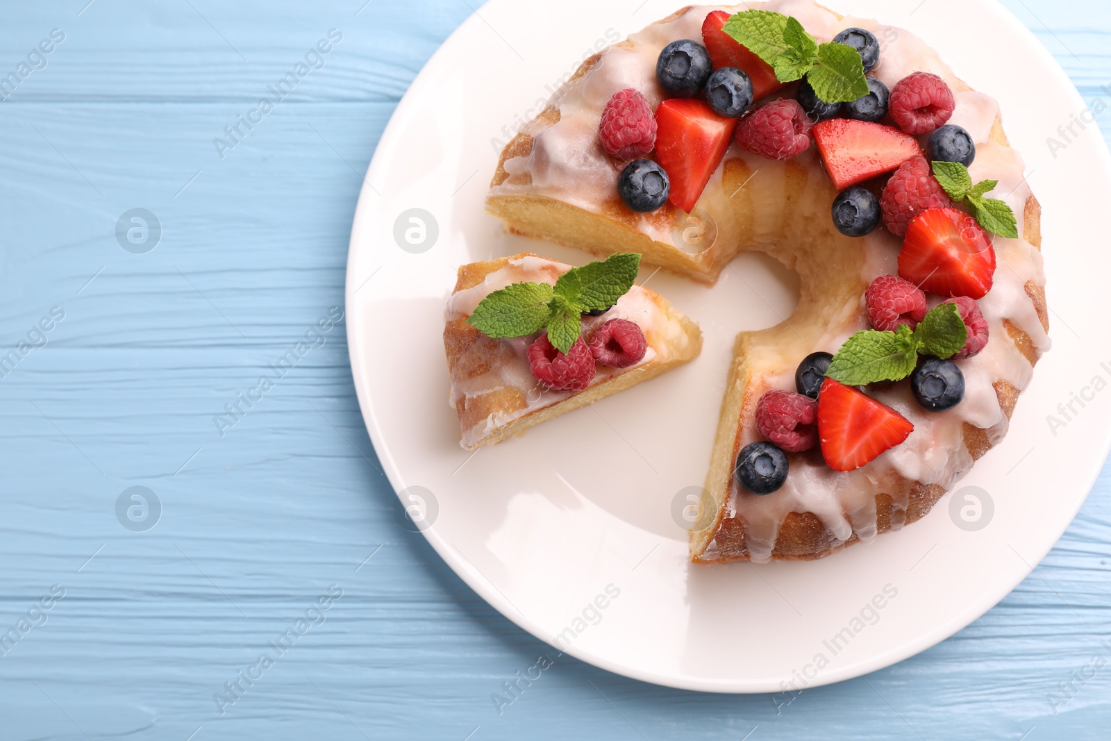 Pieces of delicious bundt cake with berries, glaze and mint on light blue wooden table, top view. Space for text Photo of Pieces of delicious bundt cake with berries, glaze and mint on light blue wooden table, top view. Space for text