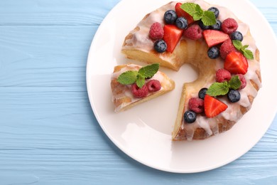 Photo of Pieces of delicious bundt cake with berries, glaze and mint on light blue wooden table, top view. Space for text