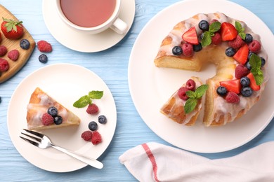 Photo of Pieces of delicious bundt cake with berries, glaze and mint served on light blue wooden table, flat lay