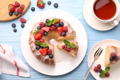 Photo of Pieces of delicious bundt cake with berries, glaze and mint served on light blue wooden table, flat lay