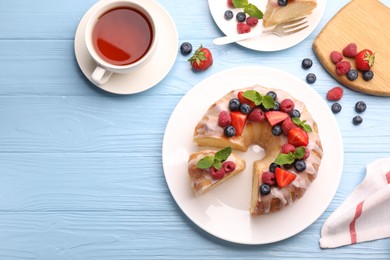 Photo of Pieces of delicious bundt cake with berries, glaze and mint served on light blue wooden table, flat lay