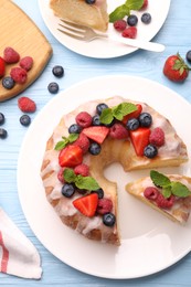 Photo of Pieces of delicious bundt cake with berries, glaze and mint served on light blue wooden table, flat lay