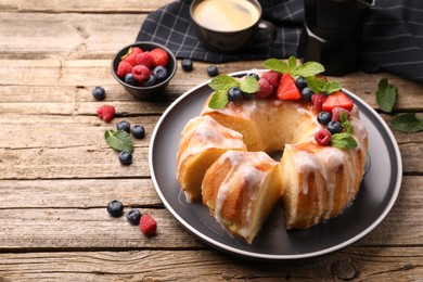 Photo of Pieces of delicious bundt cake with berries, glaze and mint on wooden table, closeup