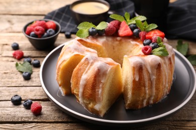 Photo of Pieces of delicious bundt cake with berries, glaze and mint on wooden table, closeup