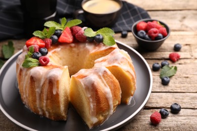 Photo of Pieces of delicious bundt cake with berries, glaze and mint on wooden table, closeup
