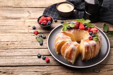 Photo of Pieces of delicious bundt cake with berries, glaze and mint on wooden table, closeup