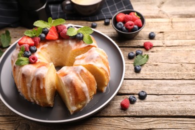 Photo of Pieces of delicious bundt cake with berries, glaze and mint on wooden table, closeup