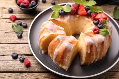 Photo of Pieces of delicious bundt cake with berries, glaze and mint on wooden table, closeup