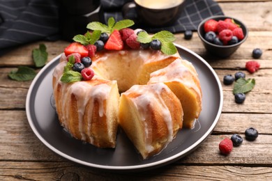 Photo of Pieces of delicious bundt cake with berries, glaze and mint on wooden table, closeup