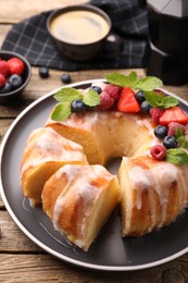 Photo of Pieces of delicious bundt cake with berries, glaze and mint on wooden table, closeup