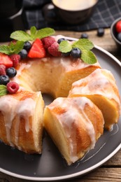 Photo of Pieces of delicious bundt cake with berries, glaze and mint on wooden table, closeup