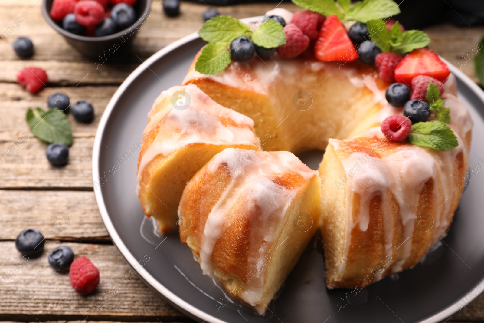 Pieces of delicious bundt cake with berries, glaze and mint on wooden table, closeup Photo of Pieces of delicious bundt cake with berries, glaze and mint on wooden table, closeup