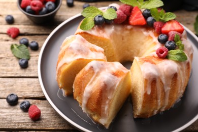 Photo of Pieces of delicious bundt cake with berries, glaze and mint on wooden table, closeup