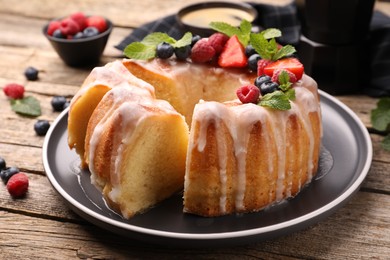Photo of Pieces of delicious bundt cake with berries, glaze and mint on wooden table, closeup