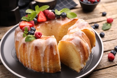 Photo of Pieces of delicious bundt cake with berries, glaze and mint on wooden table, closeup