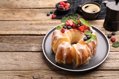 Photo of Pieces of delicious bundt cake with berries, glaze and mint on wooden table, closeup. Space for text