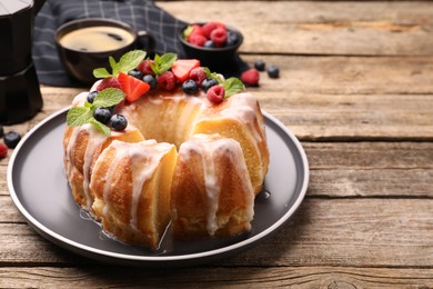 Photo of Pieces of delicious bundt cake with berries, glaze and mint on wooden table, closeup