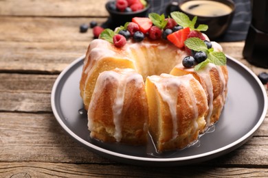 Photo of Pieces of delicious bundt cake with berries, glaze and mint on wooden table, closeup